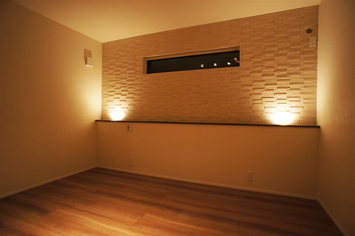 下から天井を照らす照明。通常天井に使う照明を逆に使う事により壁面の凹凸のあるタイルを美しく照らす。コストをかけず演出できるアイデア。