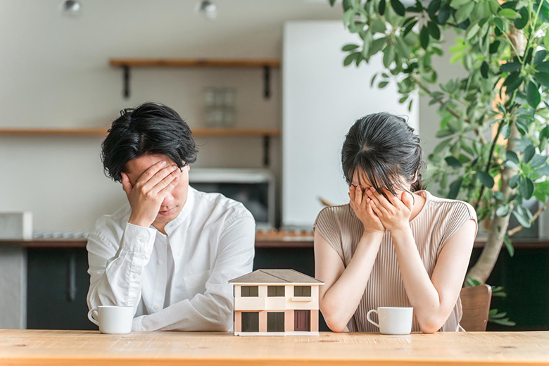 注文住宅の土地探しについて悩む夫婦と住宅模型